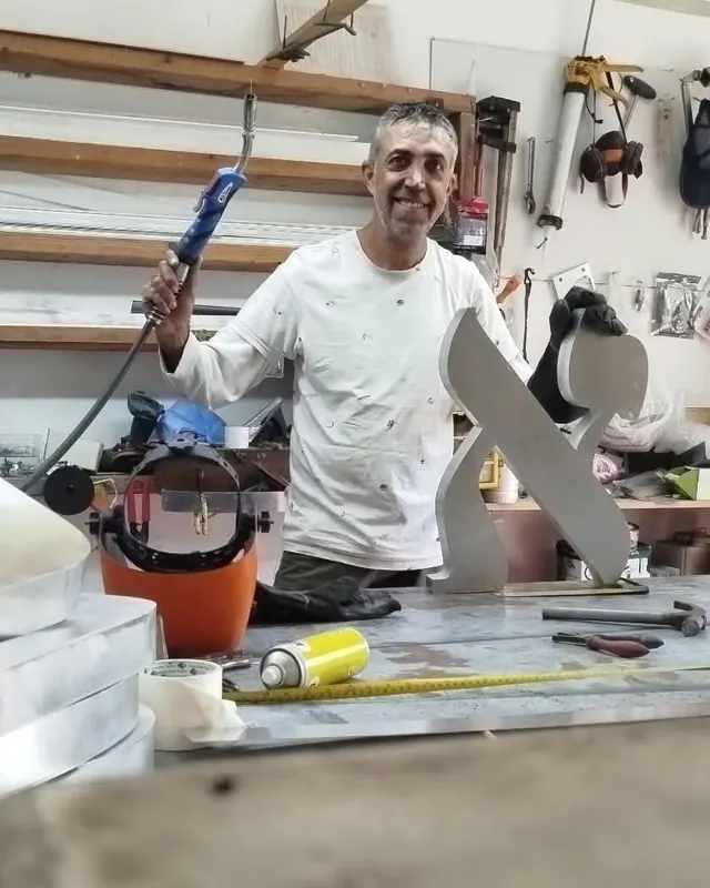 אמנון פינחסוב, מייסד כריש השלטים, בסדנה ליד אות א׳ גדולה ממתכת